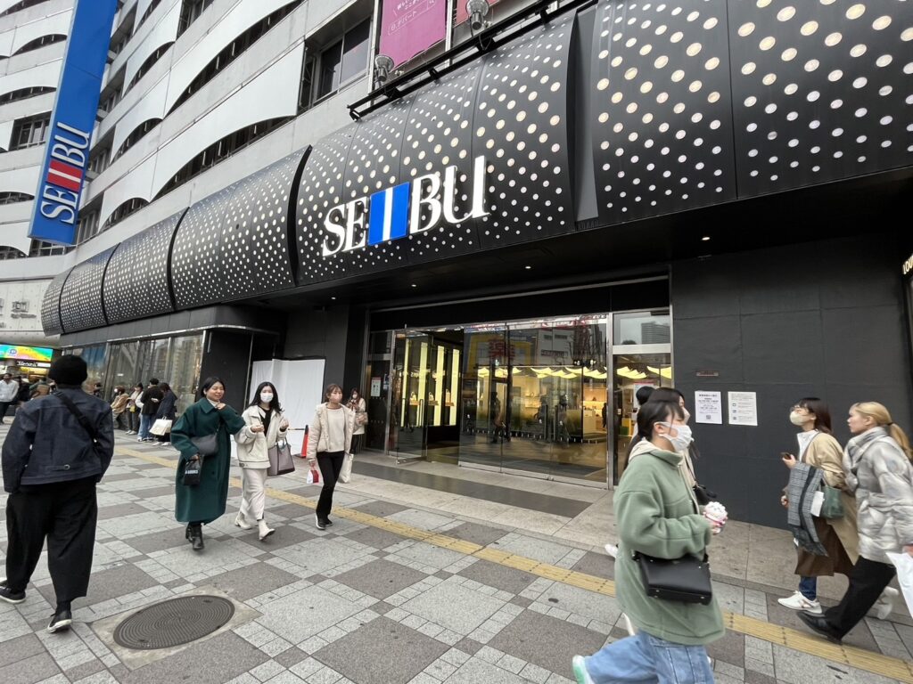 池袋駅東口の西武百貨店前の歩道と店舗入口の様子を写した写真西武池袋本店のエレベーターへ続く入口