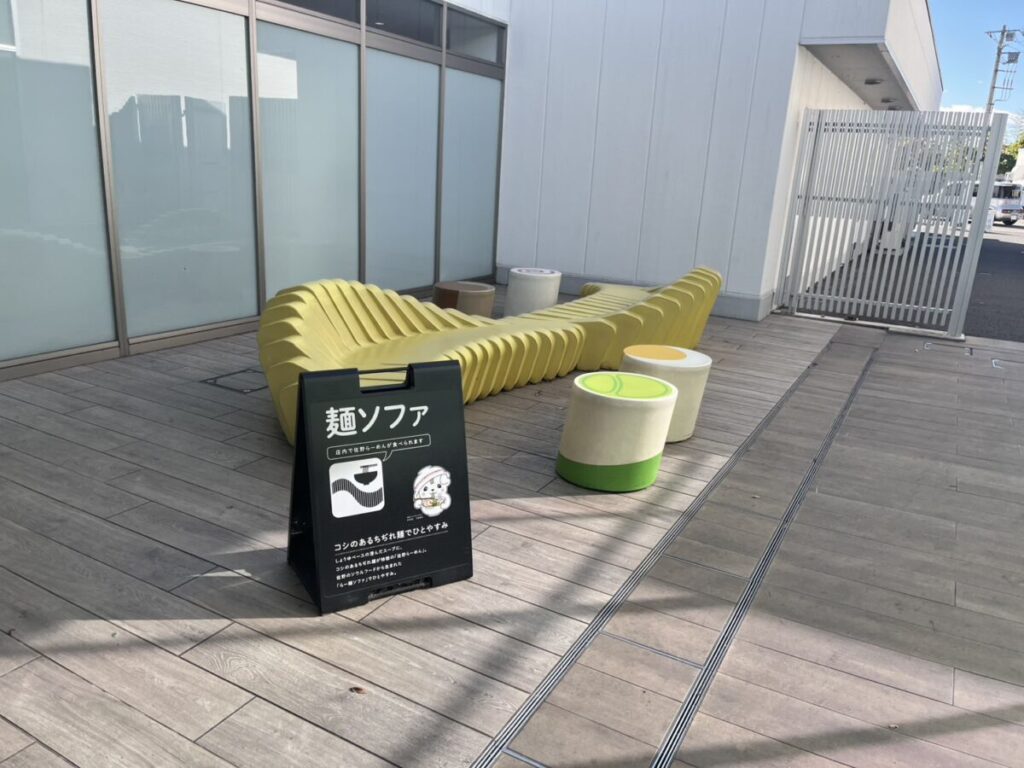 建物外側のテラスに置かれた麺ソファと丸いスツール。フードコートが混んでいても子ども連れで座って弁当を食べやすい屋外席