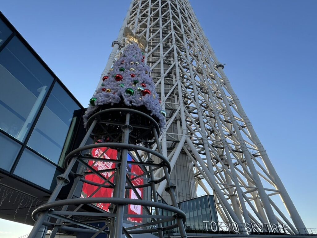 東京スカイツリーを背景にしたクリスマスマーケットのツリーと会場の様子。晴天の午後に撮影。