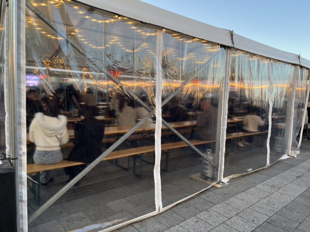 透明シートで囲まれた飲食テント席。平日午後で半分ほど埋まっている様子。