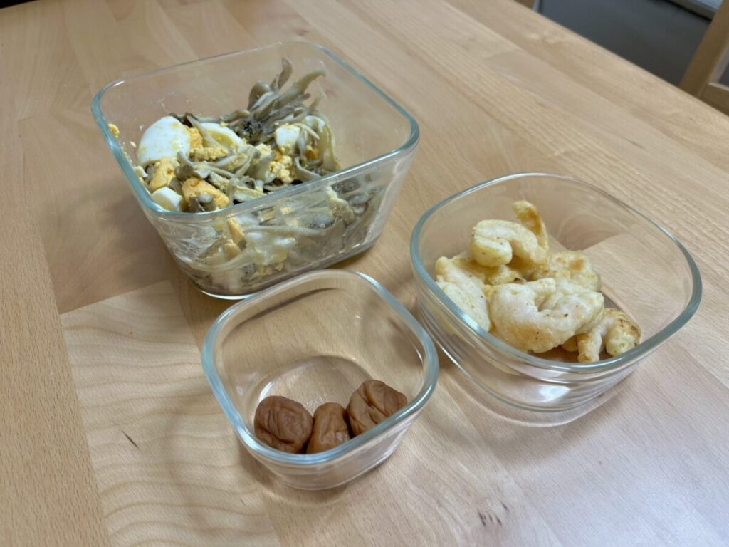 iwakiの耐熱ガラス保存容器に作り置きのおかずや梅干しを入れて食卓に置いた様子